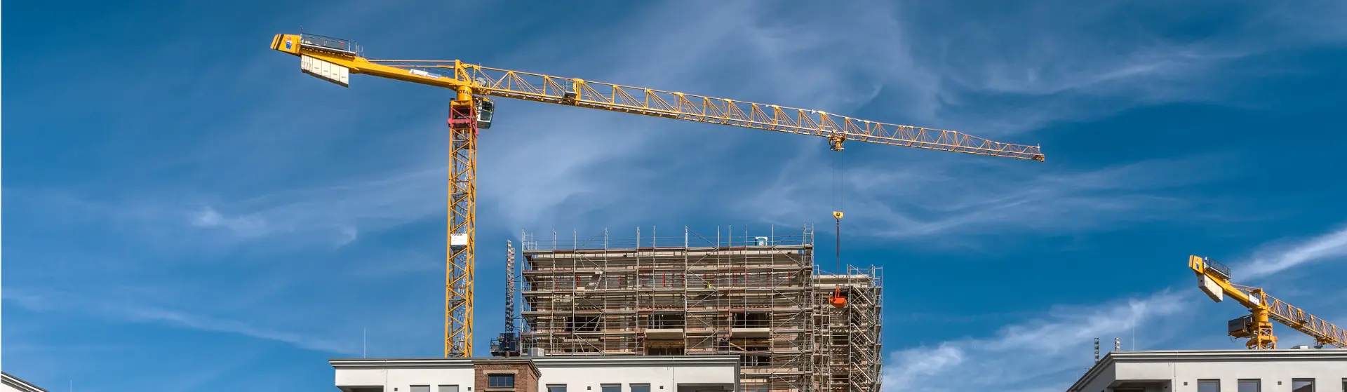 Baustelle mit zwei Baukränen und einem eingerüsteten Gebäude unter blauem Himmel