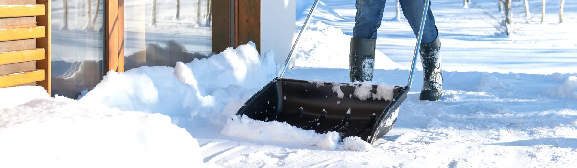 Eine Person räumt mit einer Schneeschaufel Schnee vor einem Haus weg